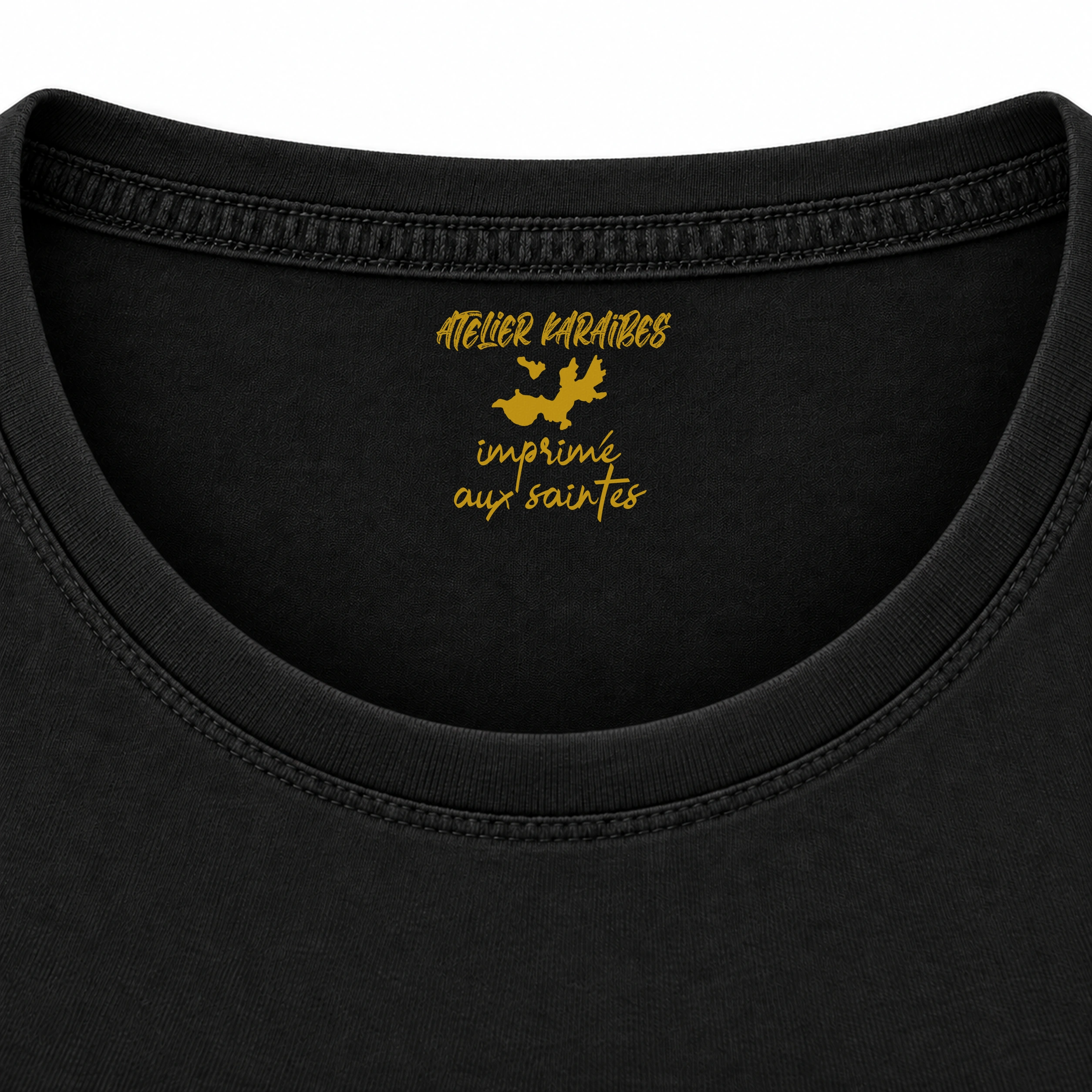 Étiquette intérieure Atelier Karaïbes « imprimé aux Saintes » en jaune moutarde sur le T-shirt rouloté noir