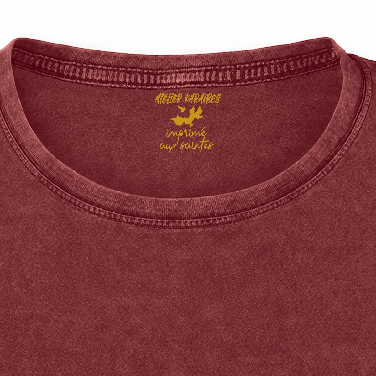 Gros plan de la signature intérieure Atelier Karaïbes imprimée en jaune moutarde sous le col du T-shirt vieilli femme rouge grenat délavé