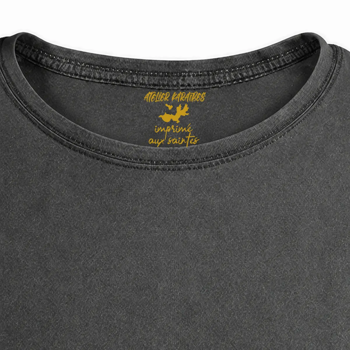 Gros plan de la signature intérieure Atelier Karaïbes imprimée en jaune moutarde sous le col du T-shirt vieilli homme gris anthracite délavé